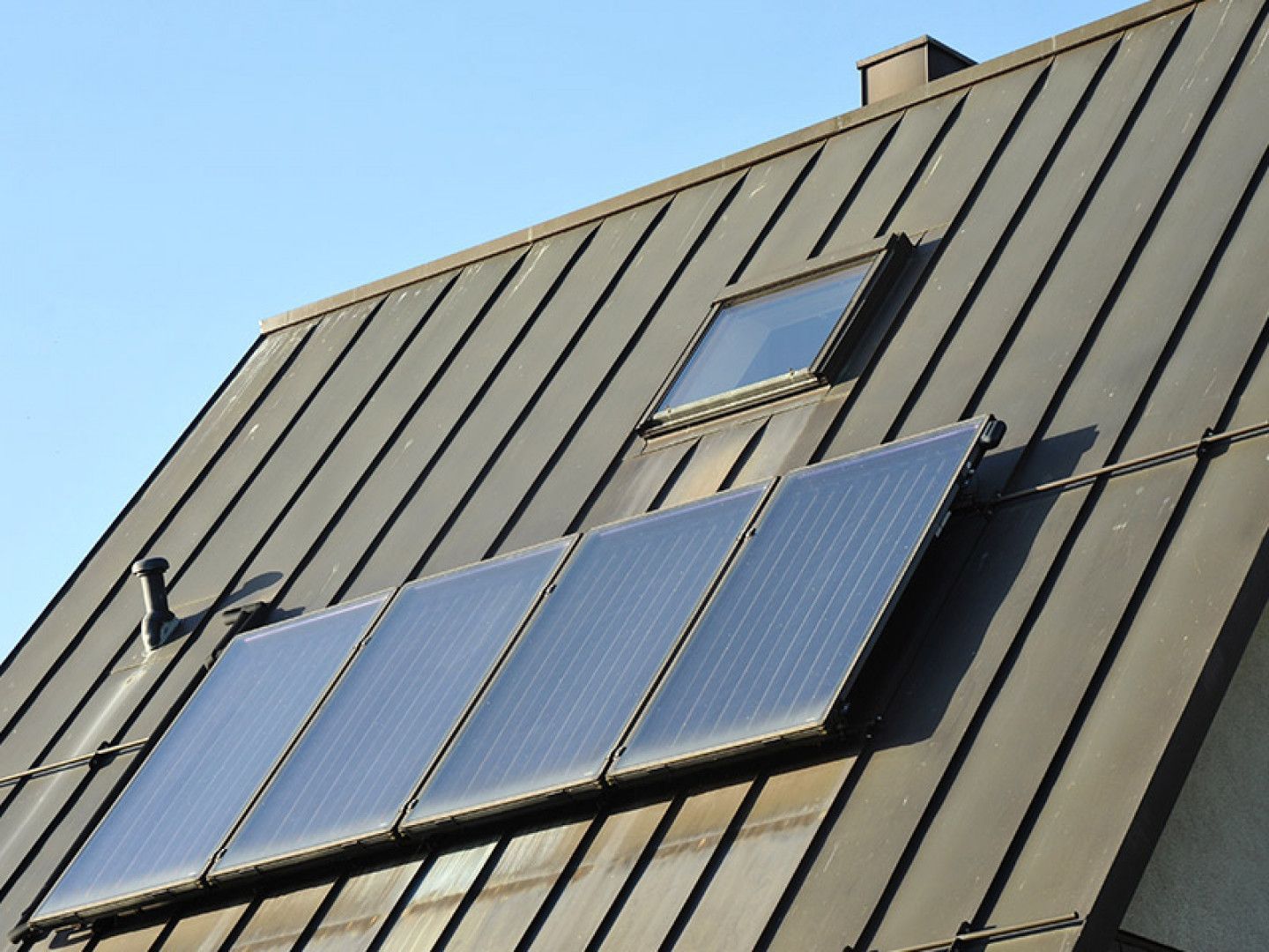 Solar panels mounted on a sloped gray roof with a skylight under a blue sky