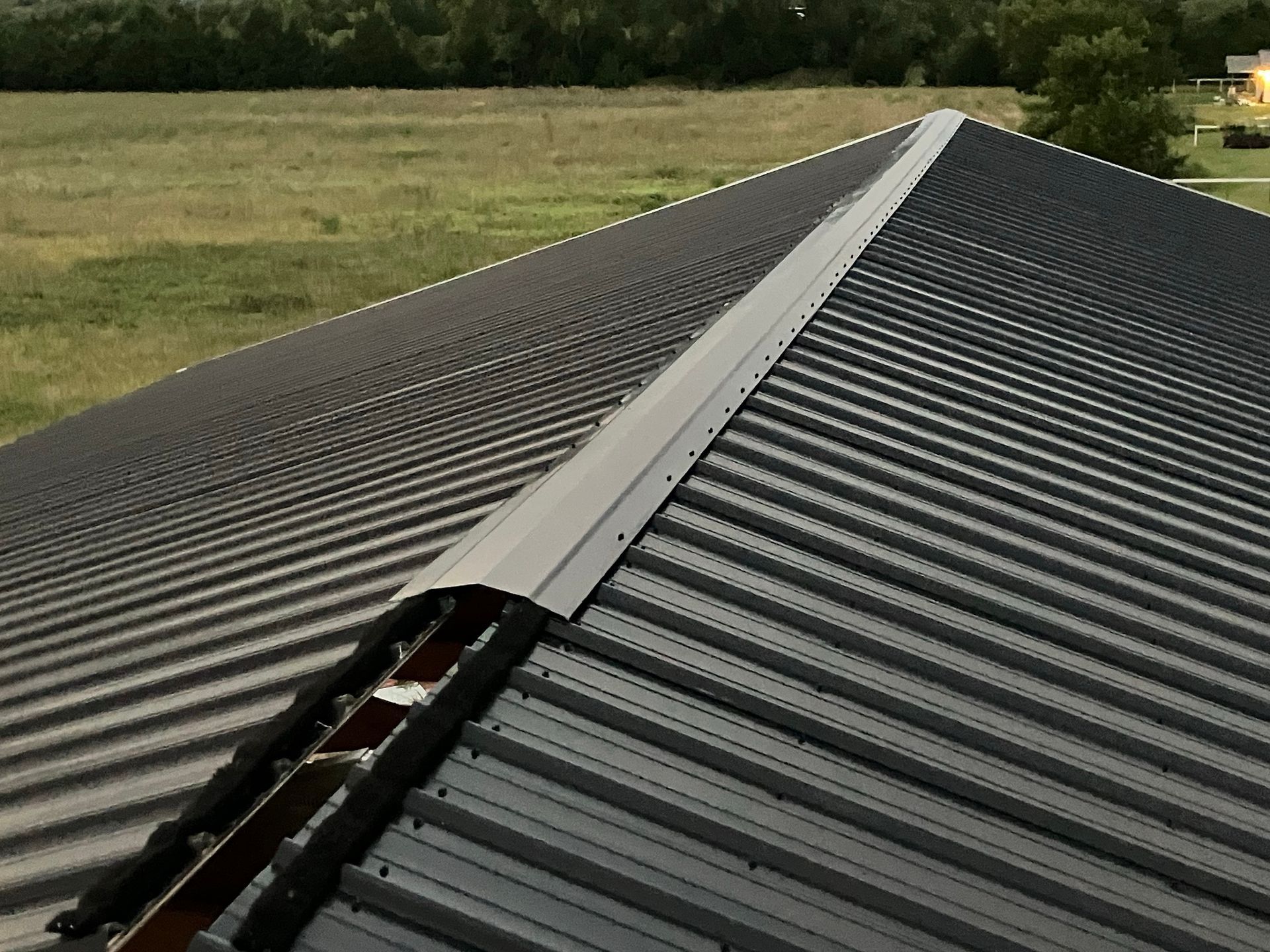 Long corrugated metal roof with a central ridge line, viewed across a grassy field