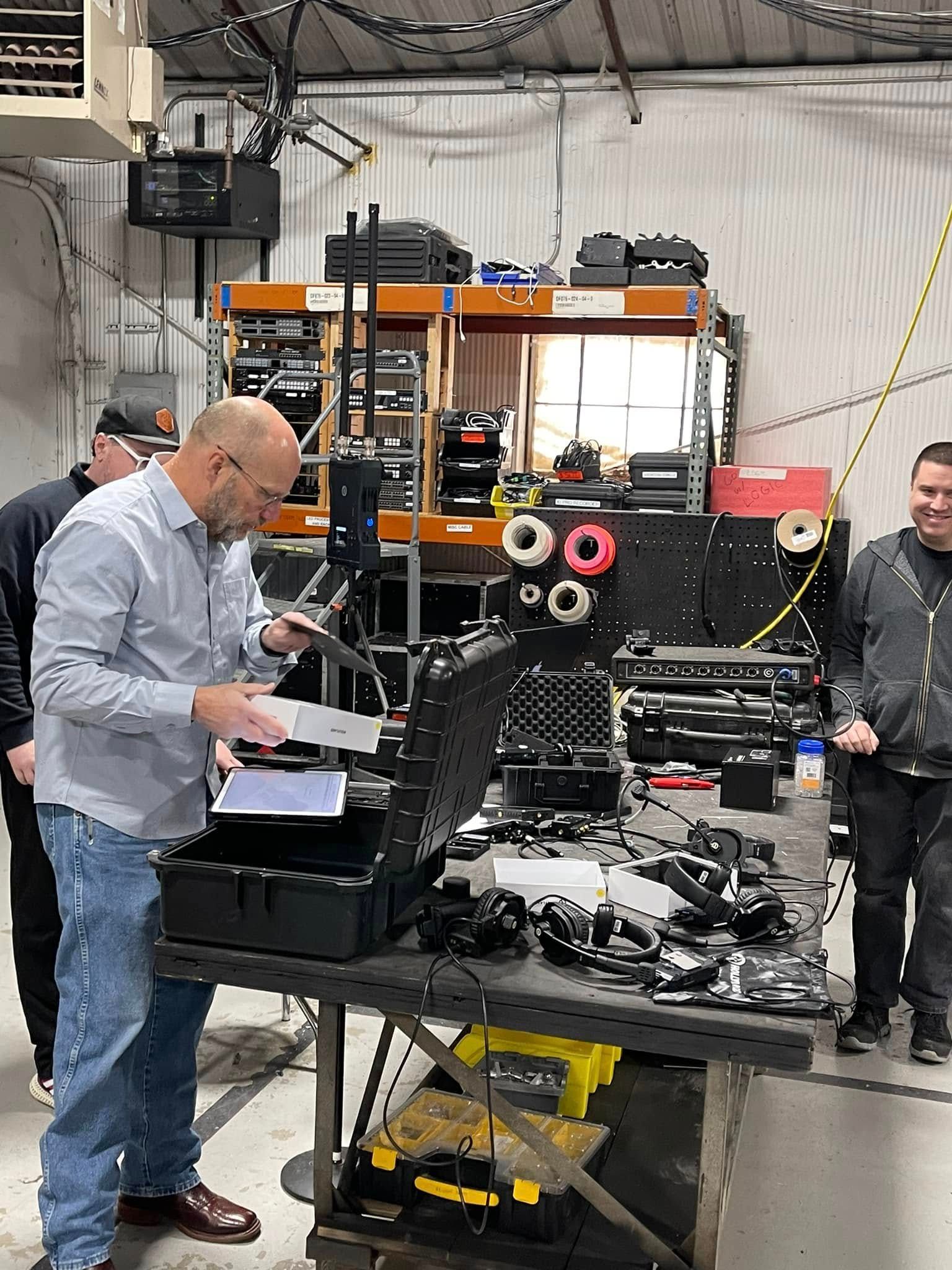 Men assembling equipment in a warehouse. One man examines a device, others observe, industrial setting.