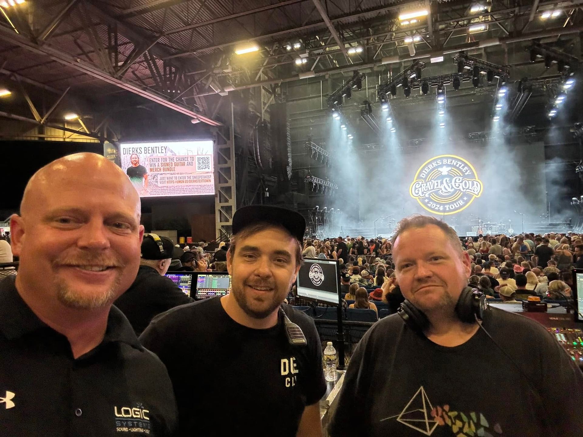 Three men smiling in front of a stage with a crowd, with the stage logo visible.