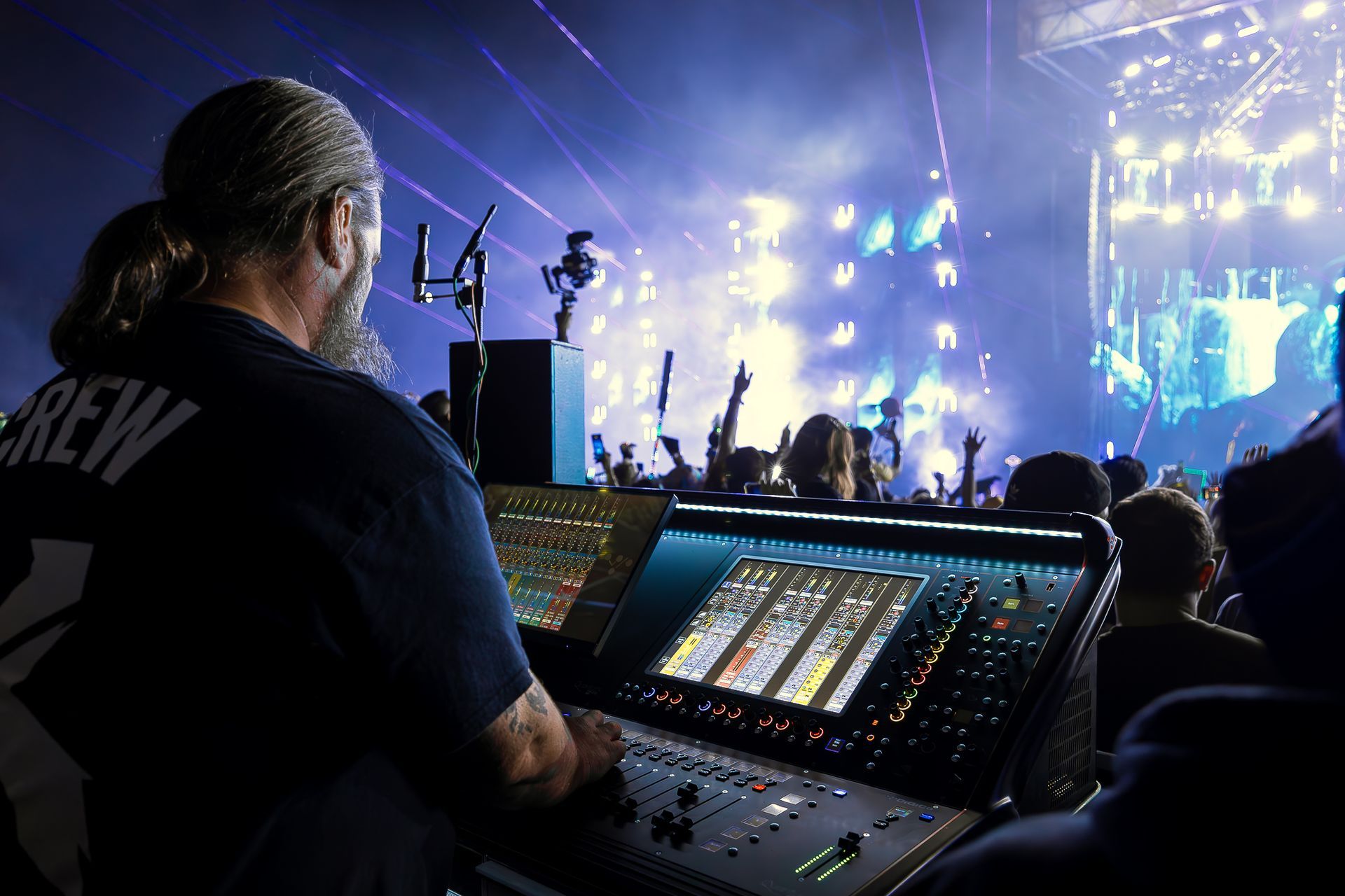 Woman with blue hair stands next to sound equipment at an outdoor concert.
