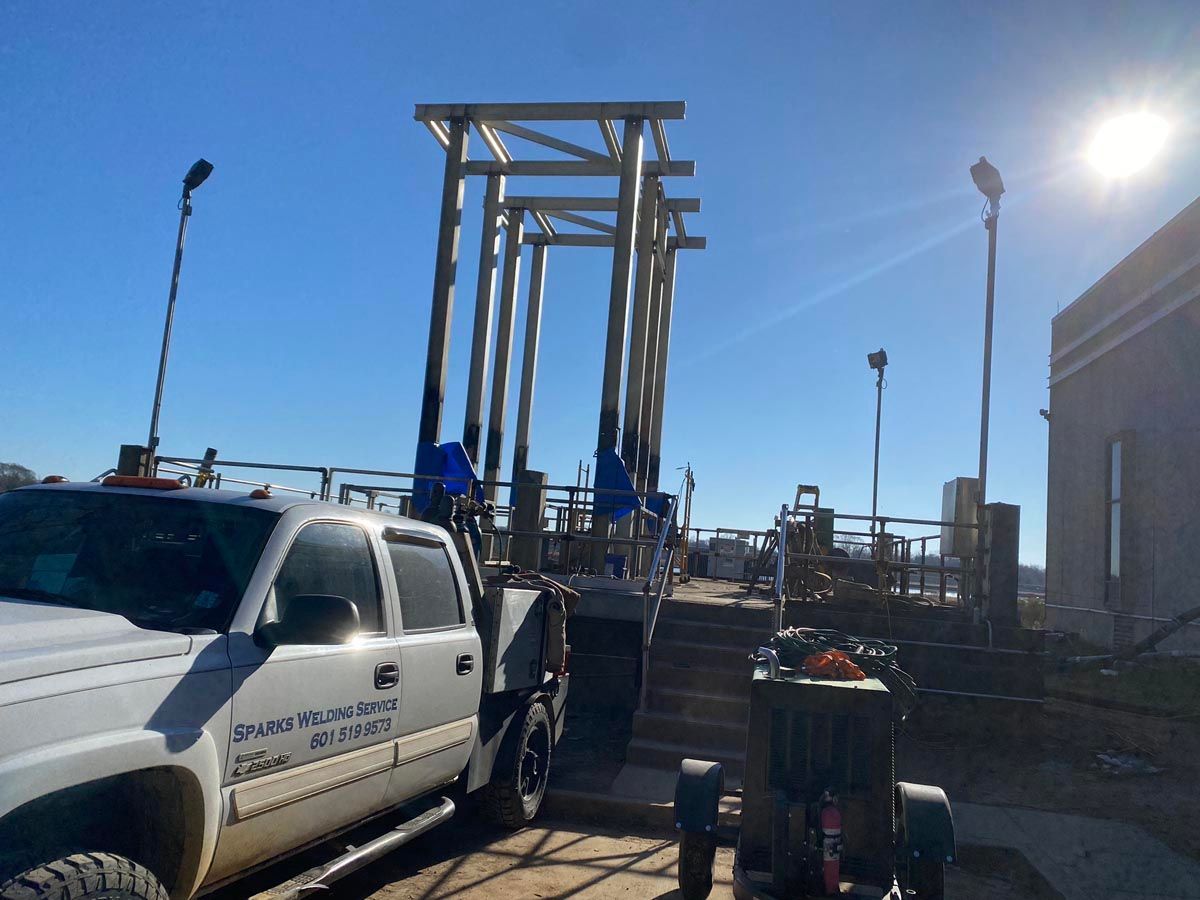 A white work truck parked near a construction site with steel scaffolding frame under a clear blue sky.