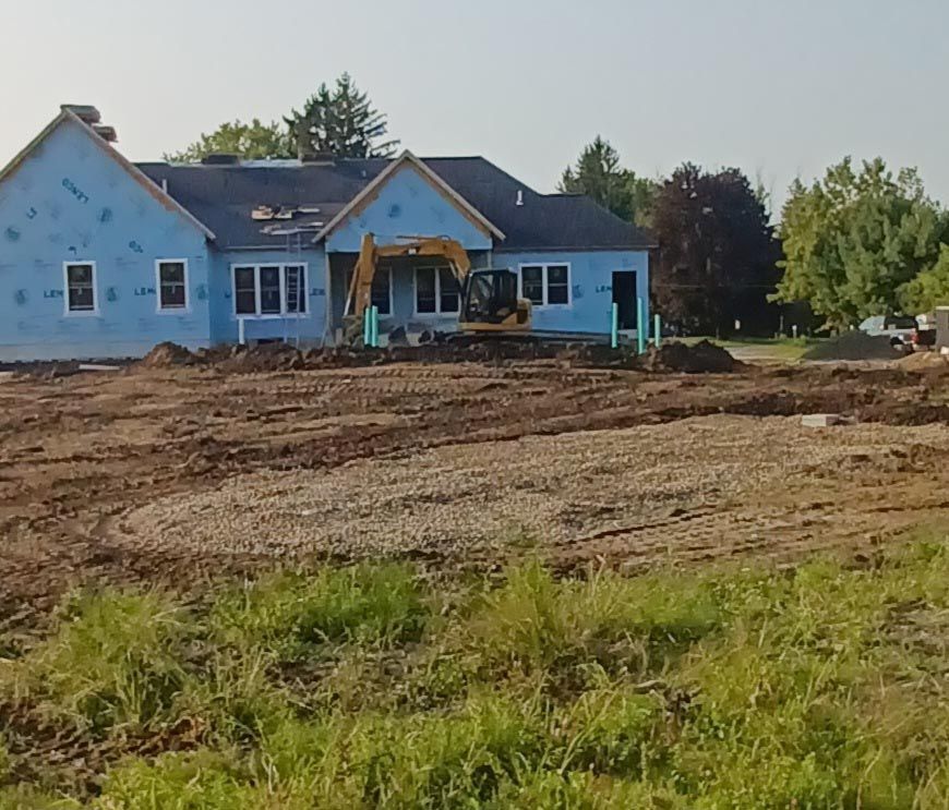 A house is being built in a field with a bulldozer in front of it.