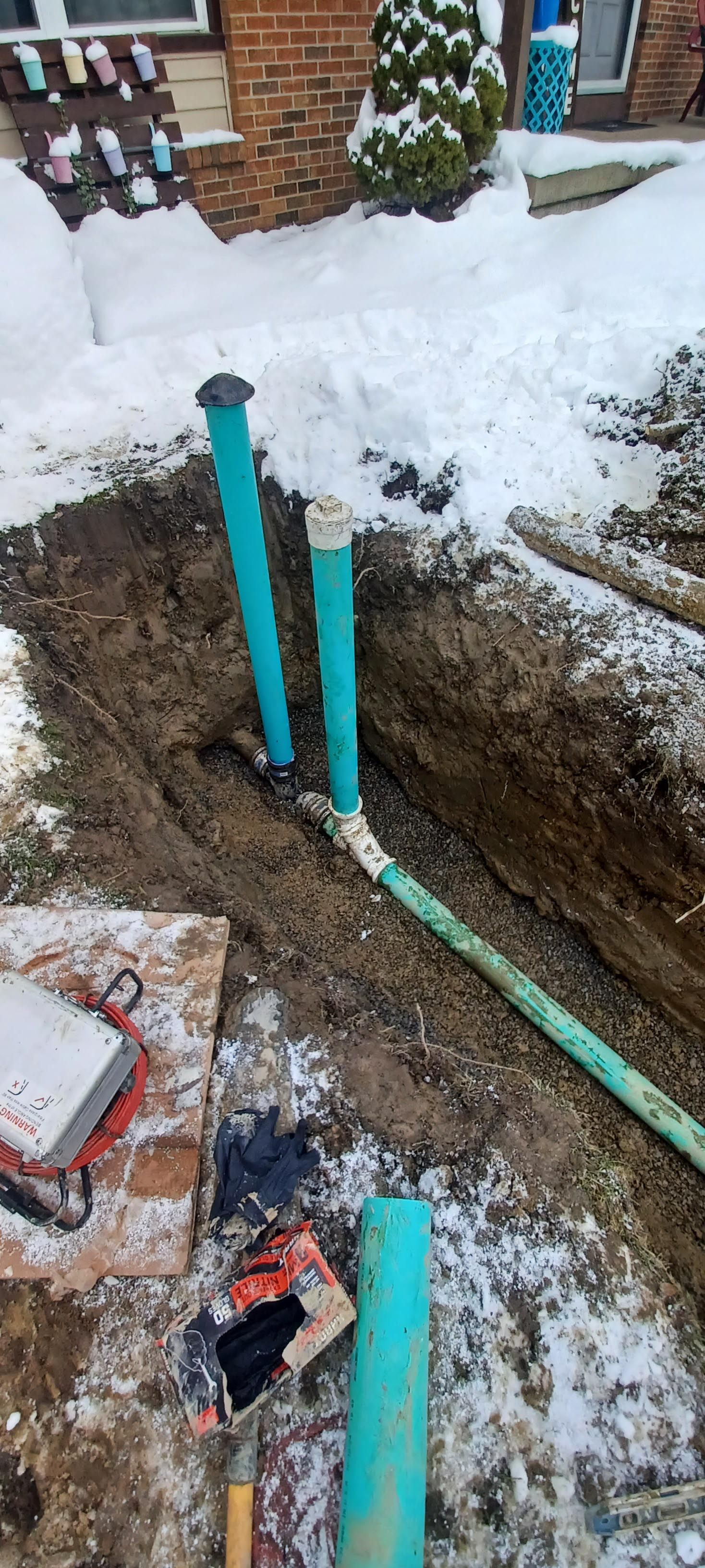 A bunch of pipes are laying in the dirt in front of a house.