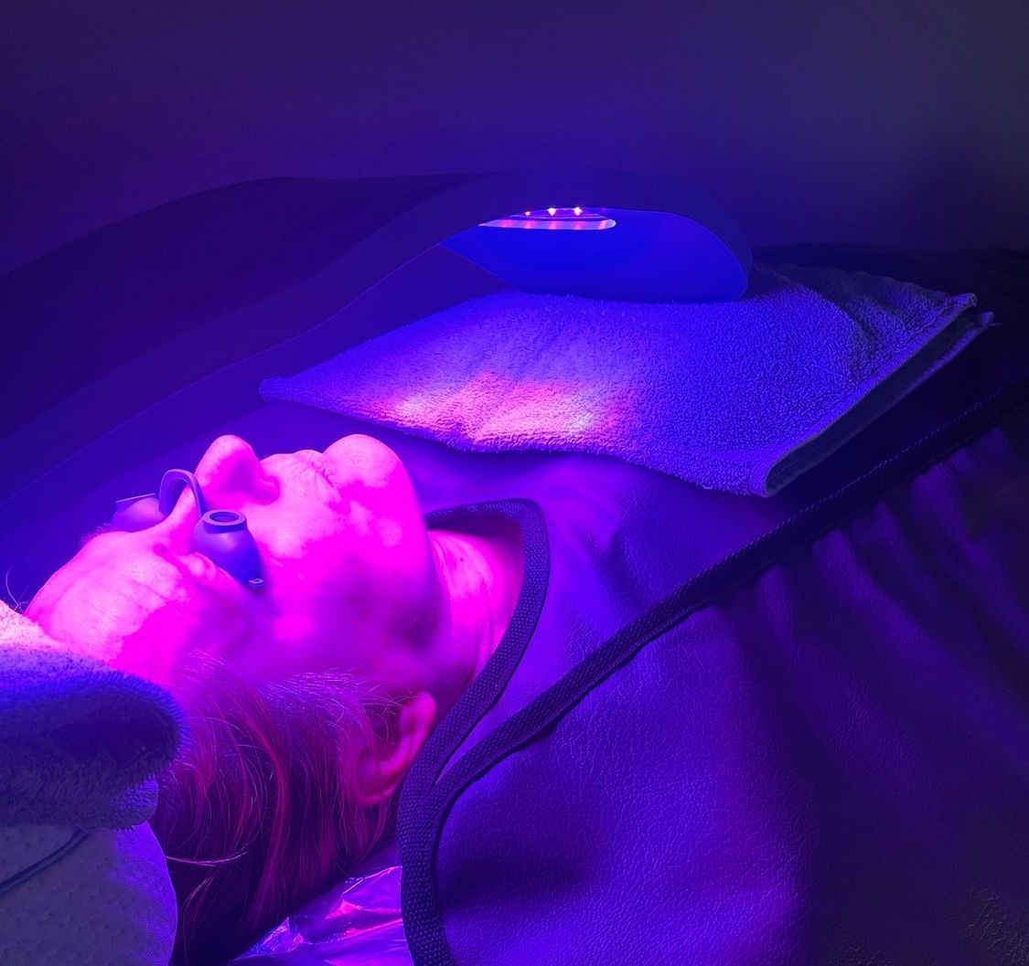A person is laying on a bed with purple lights on their face.