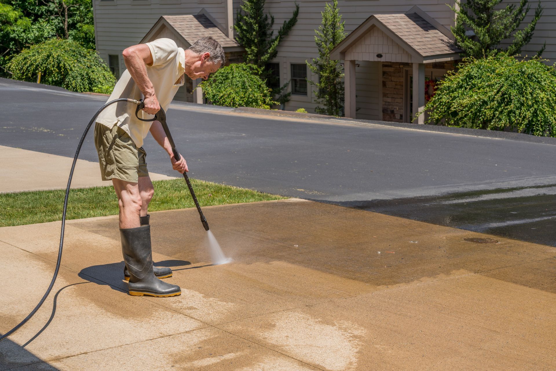 A man is using a high pressure washer to clean a sidewalk.