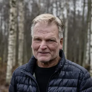 A man in a black jacket is standing in the woods.