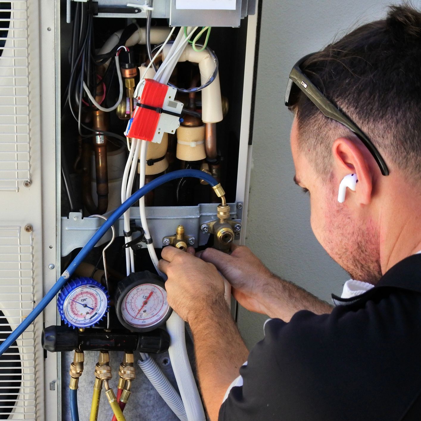 A man wearing ear buds is working on an air conditioner