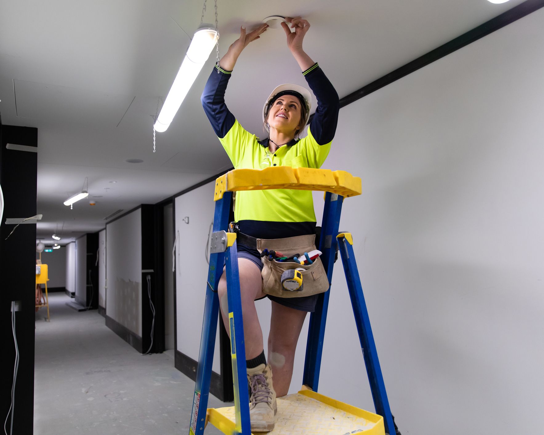 A woman is standing on a ladder fixing a light on the ceiling.