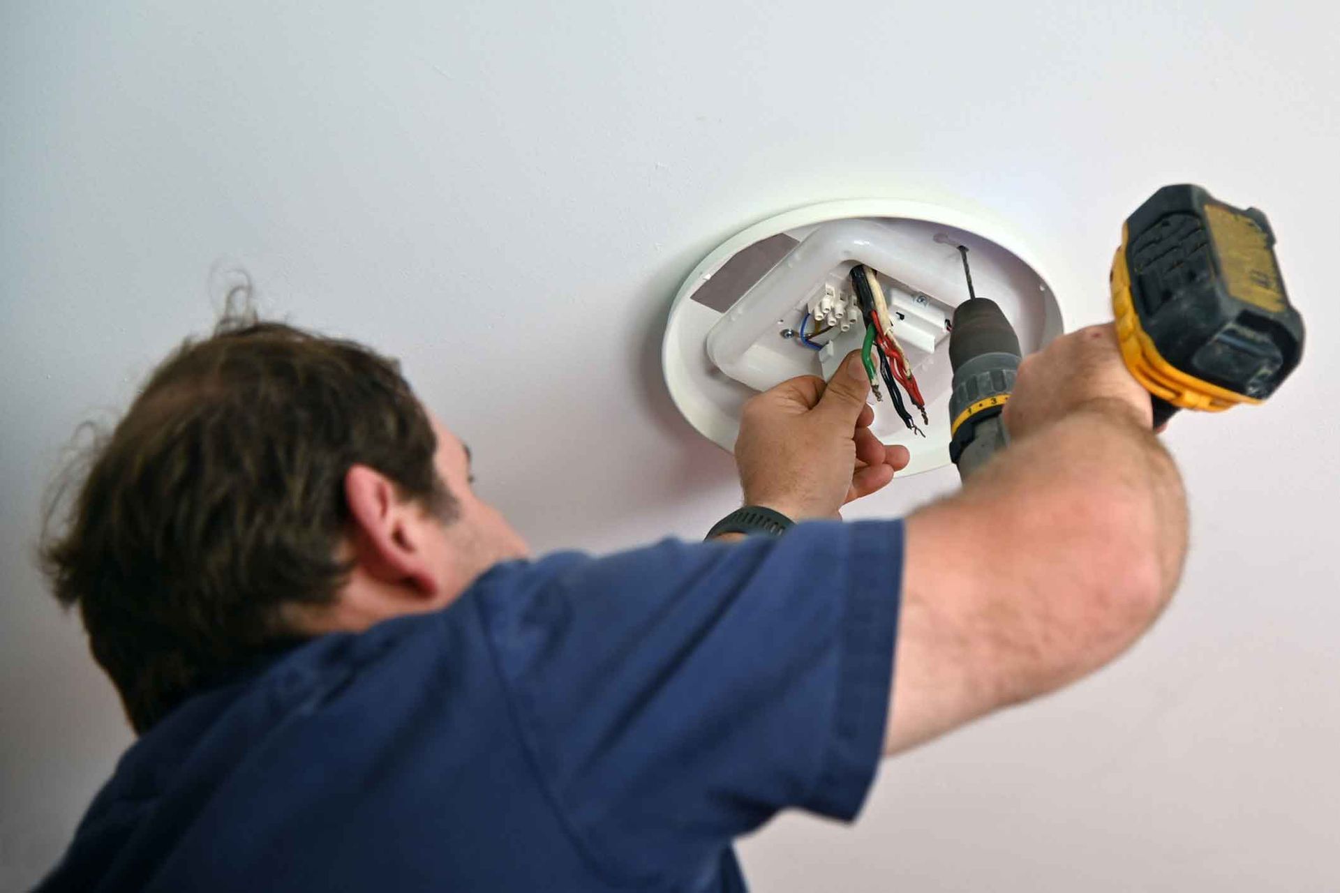 A man is using a drill to install a light fixture on the ceiling.
