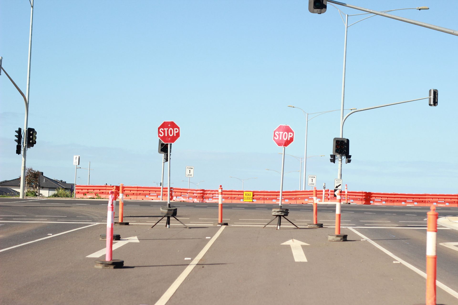 Road blocked by orange barriers with stop signs at a clear intersection.