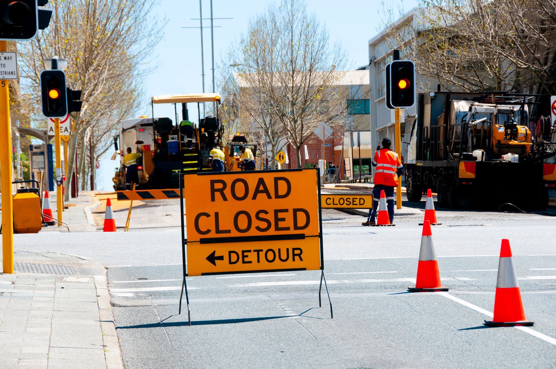 Road closed detour sign with traffic cones and construction equipment blocking the street