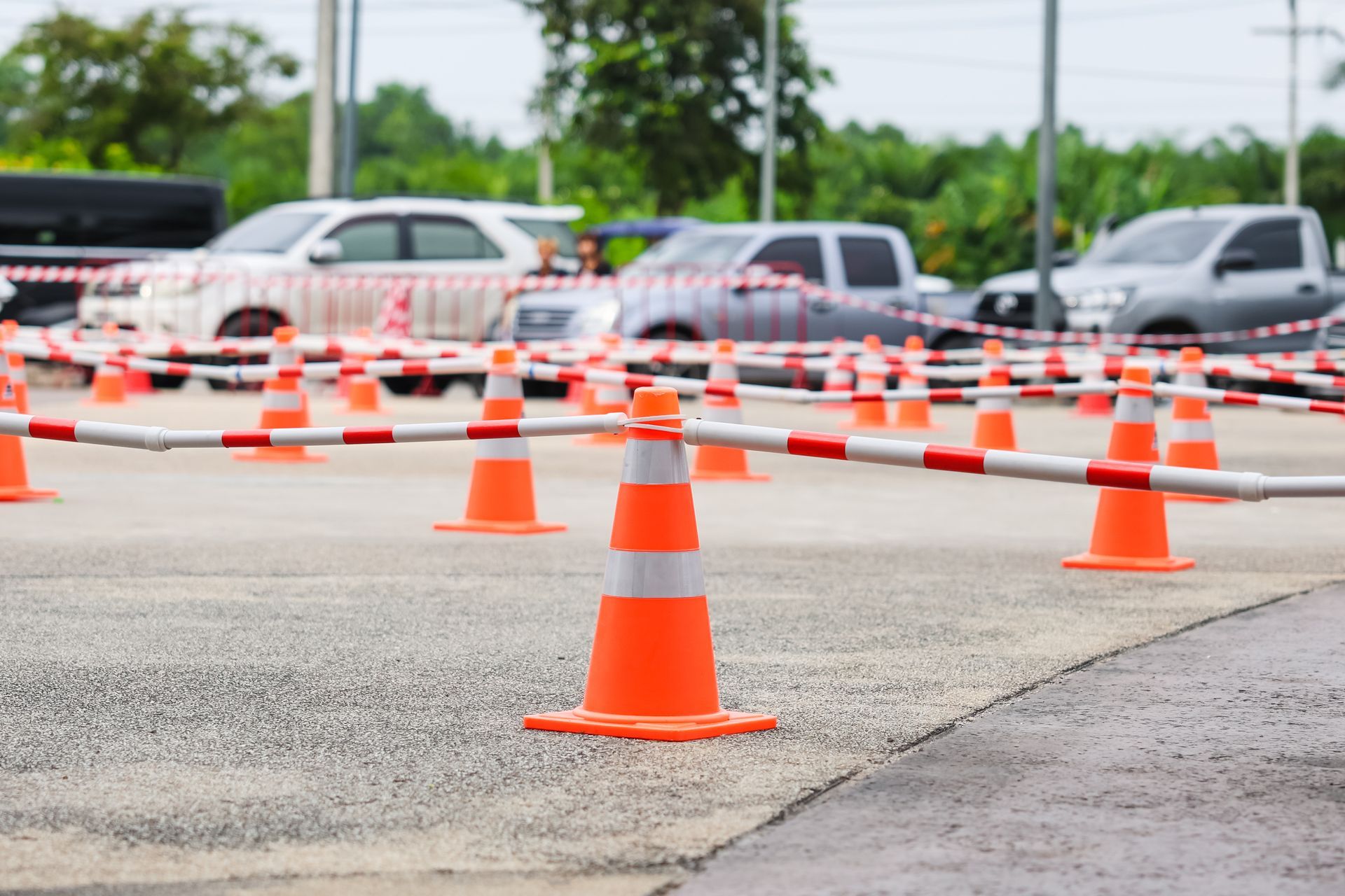 Orange traffic cones marking a barricaded parking lot with cars in the background