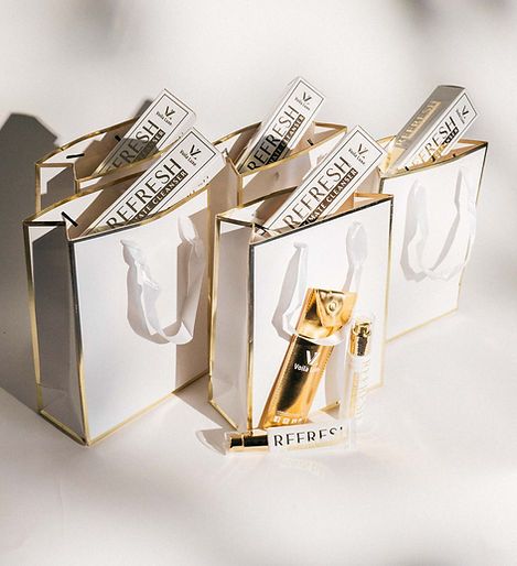 White and gold gift bags with “Fresh” makeup boxes and a lip gloss tube displayed on a light surface