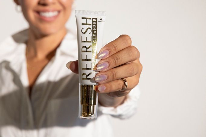 Person holding a tube labeled “REFRESH” toward the camera in a bright setting