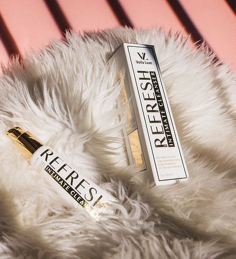 Two REFRESH lip gloss tubes on white faux fur against a pink background.