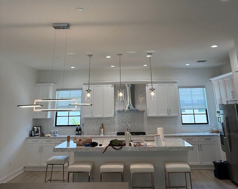 A kitchen with white cabinets , a large island , stools and a refrigerator.