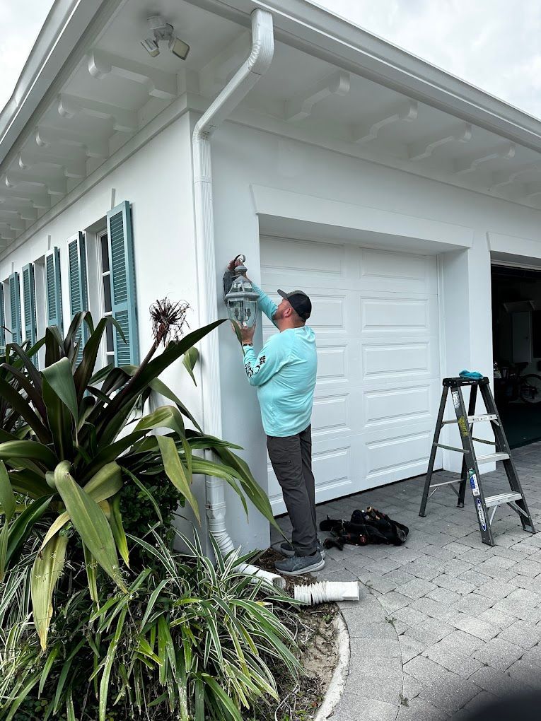 A man is fixing a light on the side of a house.