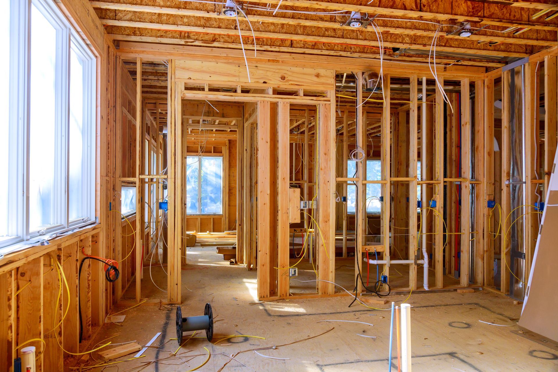 Interior of a house under construction; wooden framing, electrical wiring, and windows.