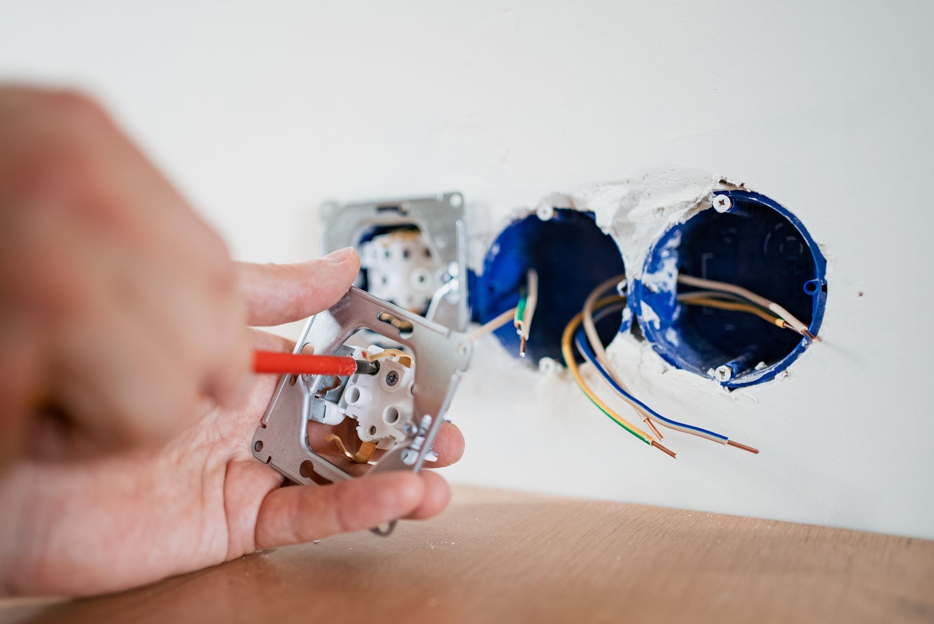Person using a screwdriver to install an electrical outlet. Wires and outlet boxes are visible.