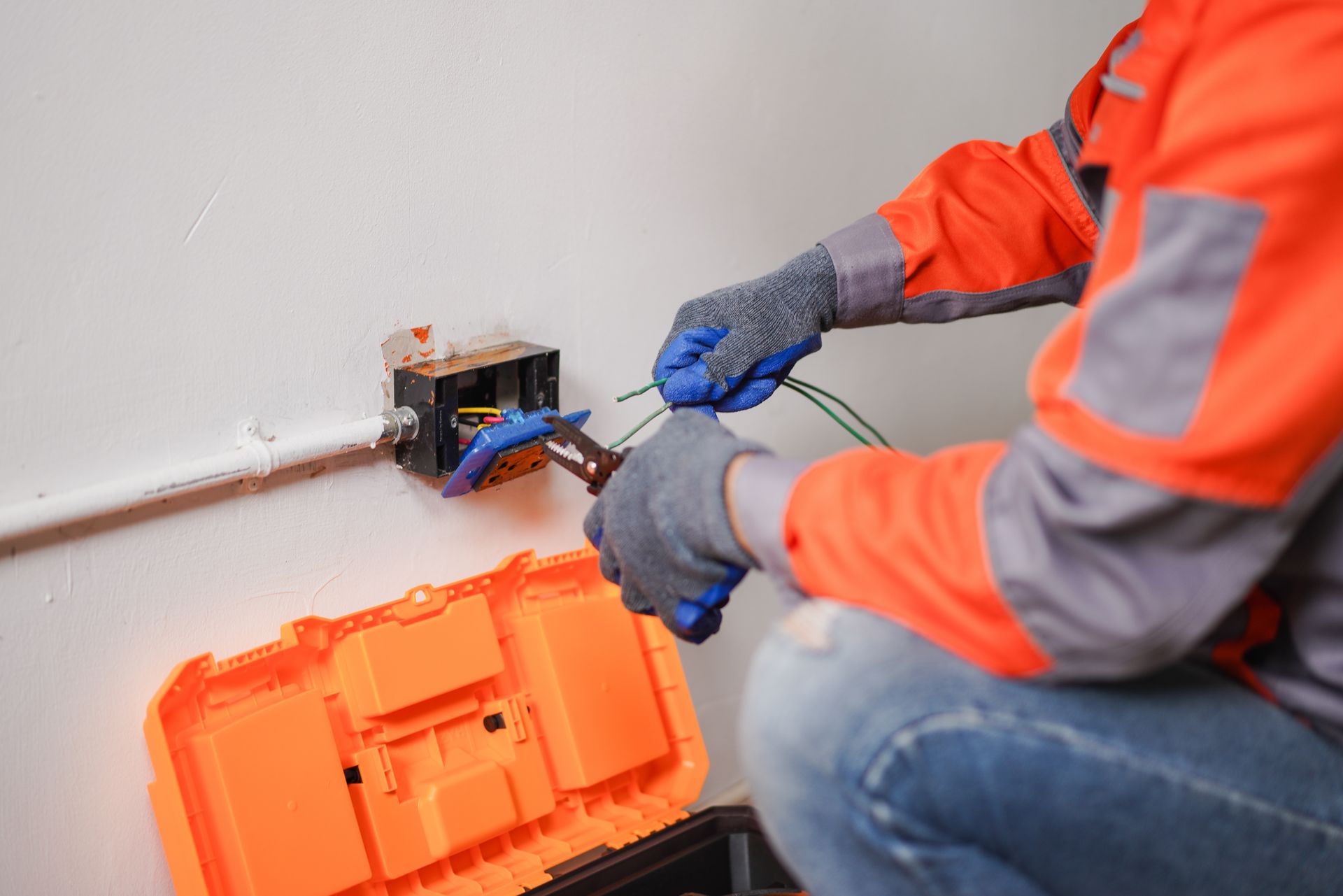 Person using wire strippers on electrical wires outside a white building.