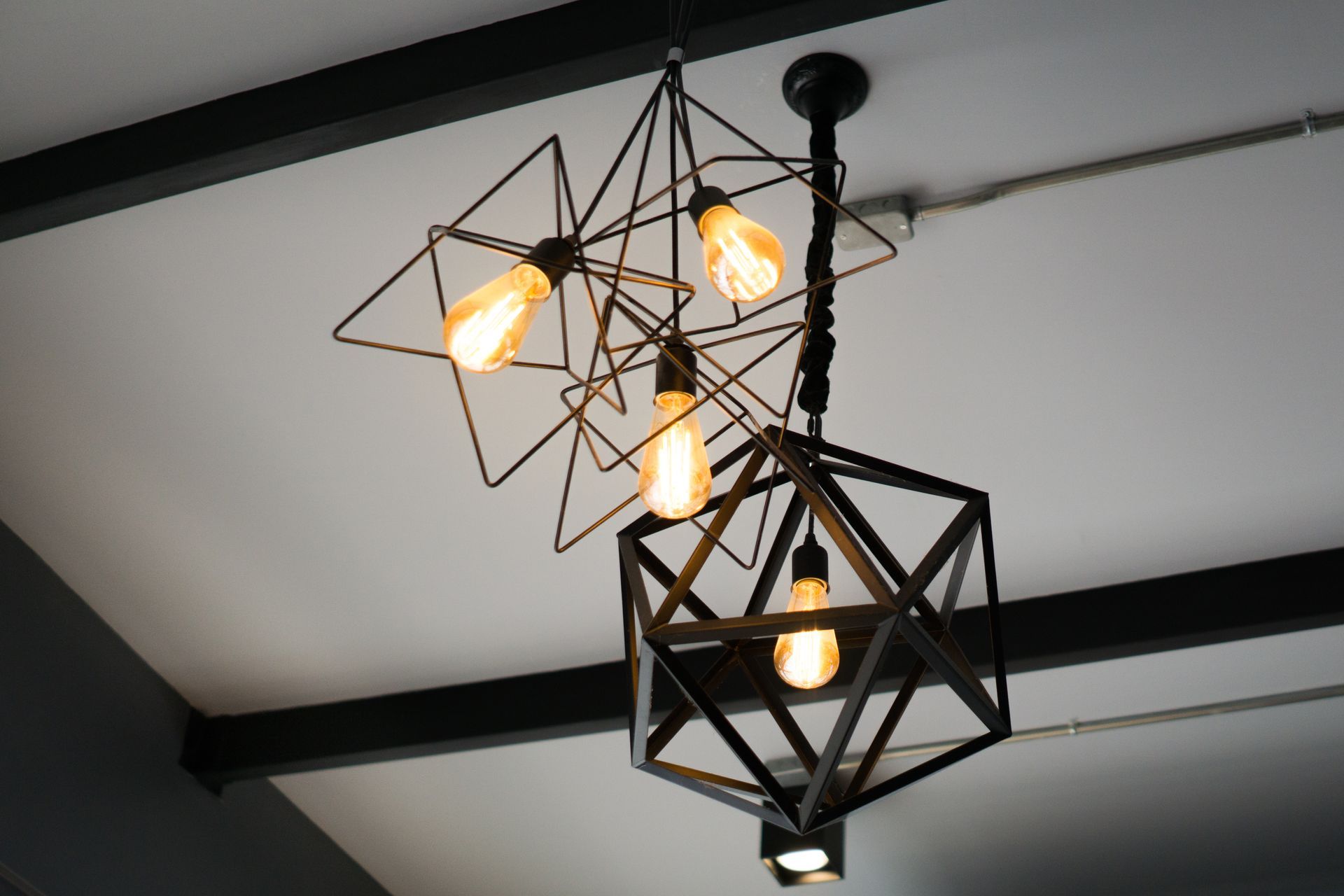 Geometric black metal pendant lights with Edison bulbs hanging from a white ceiling.