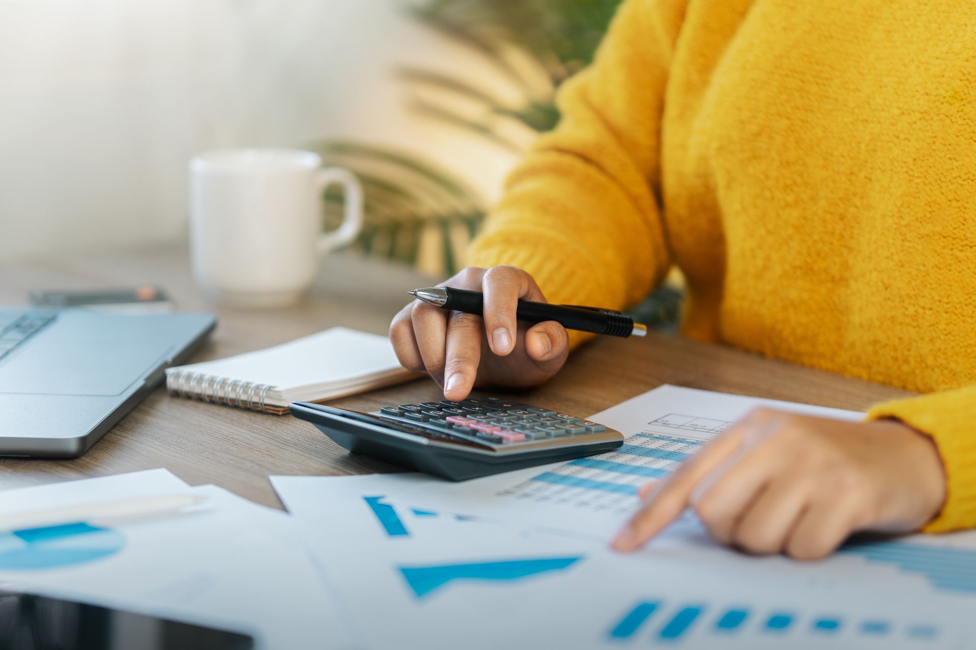 A woman is sitting at a table using a calculator and a pen.