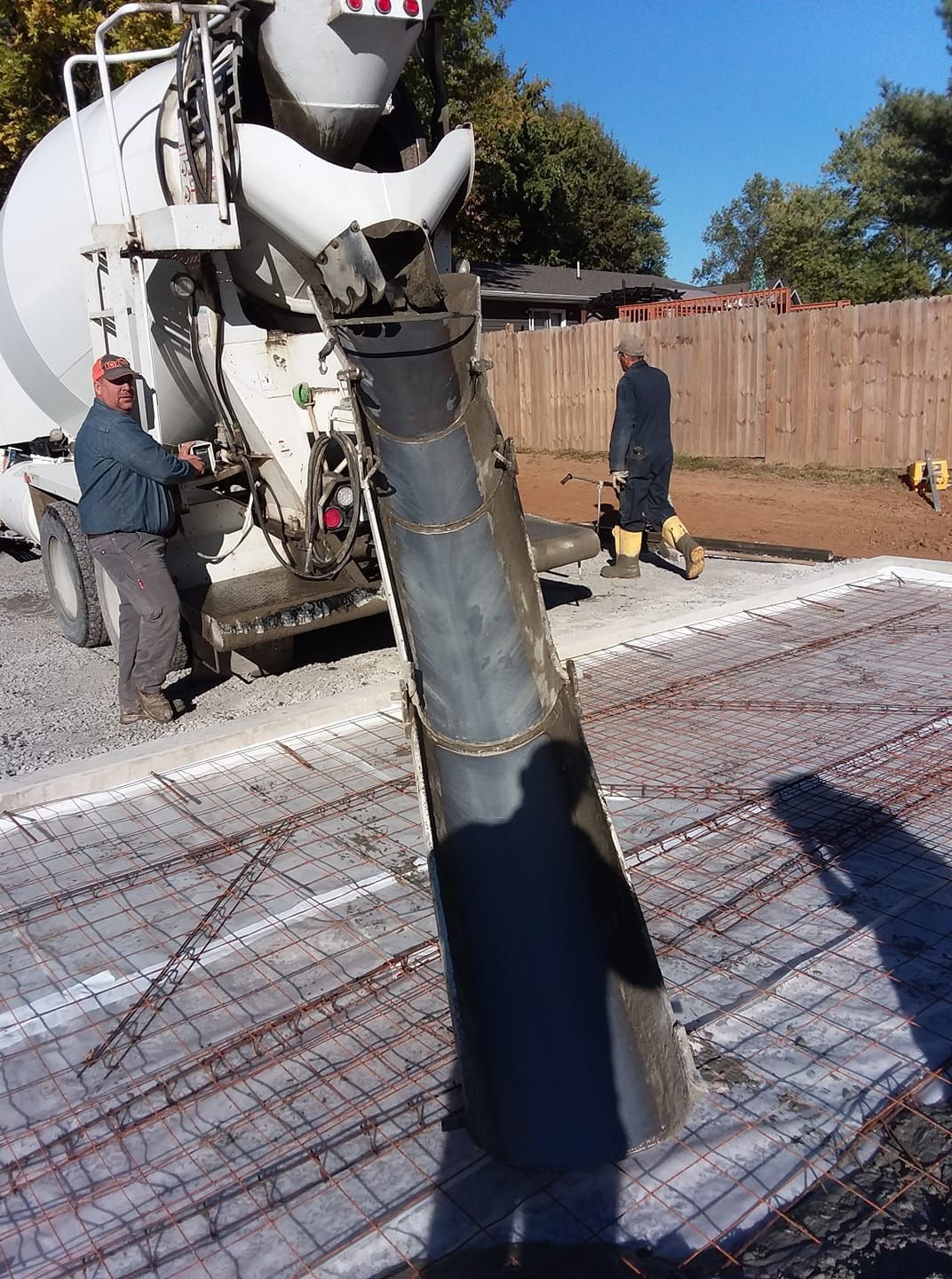 A concrete truck pours wet cement down a chute onto a wire-mesh prepared base in an outdoor construction site.