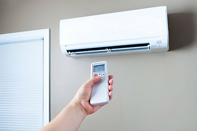 A person is holding a remote control in front of an air conditioner.