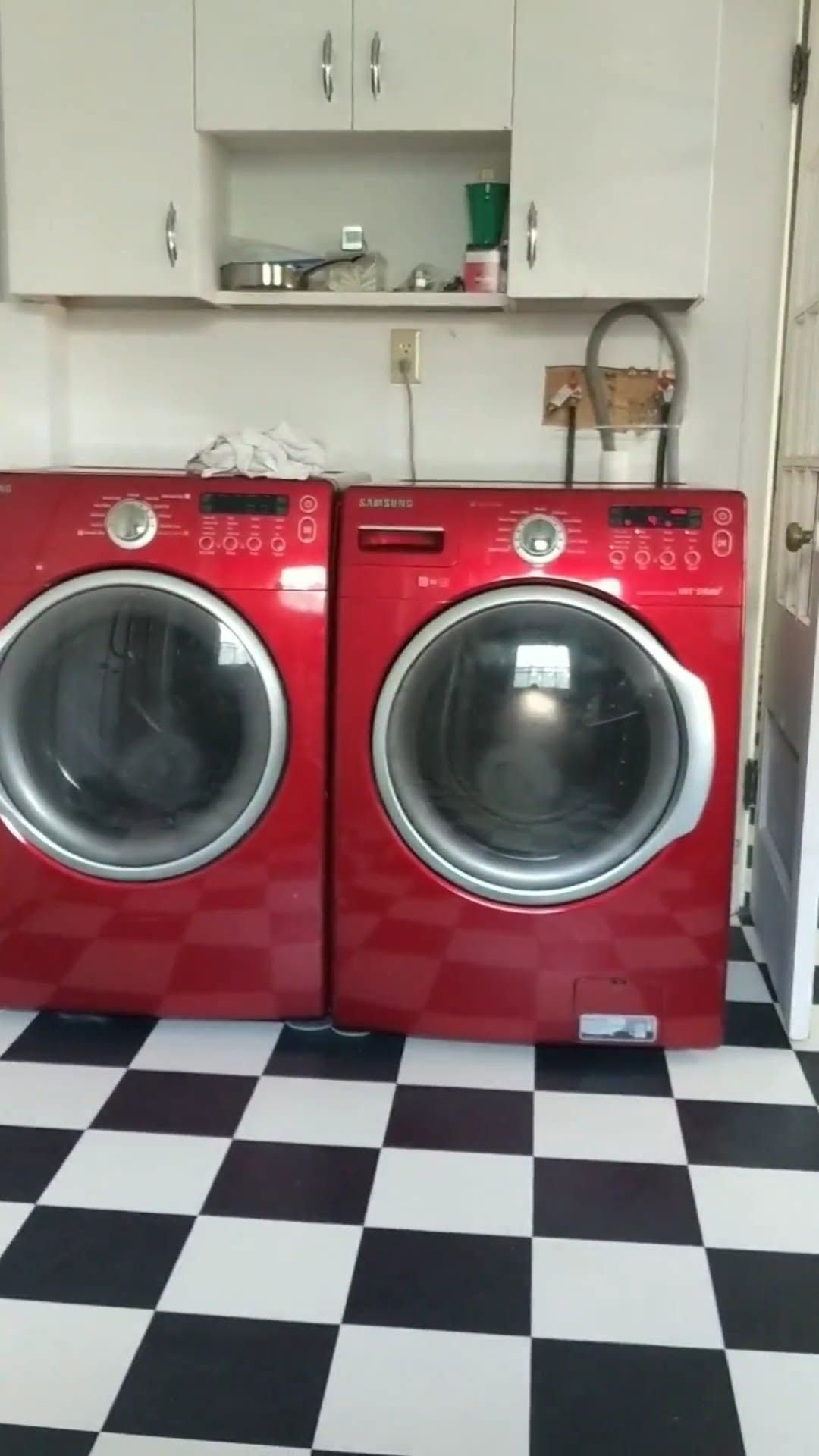 Red laundry room with a washer and dryer under white cabinets, on a black-and-white checkered floor