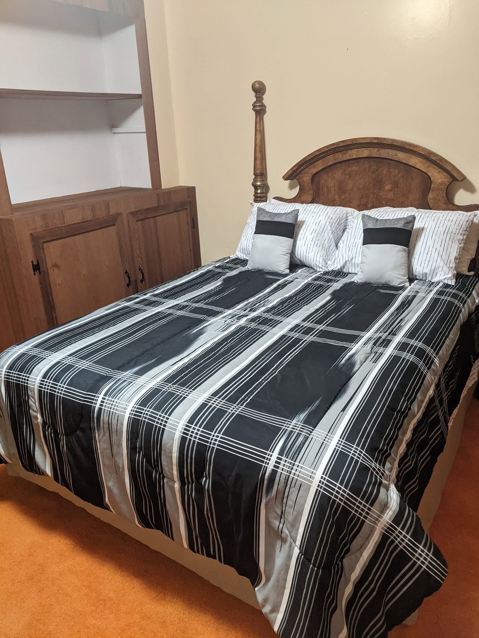 Bedroom with a wooden bed, black-and-white patterned bedspread, and matching pillows next to a cabinet.