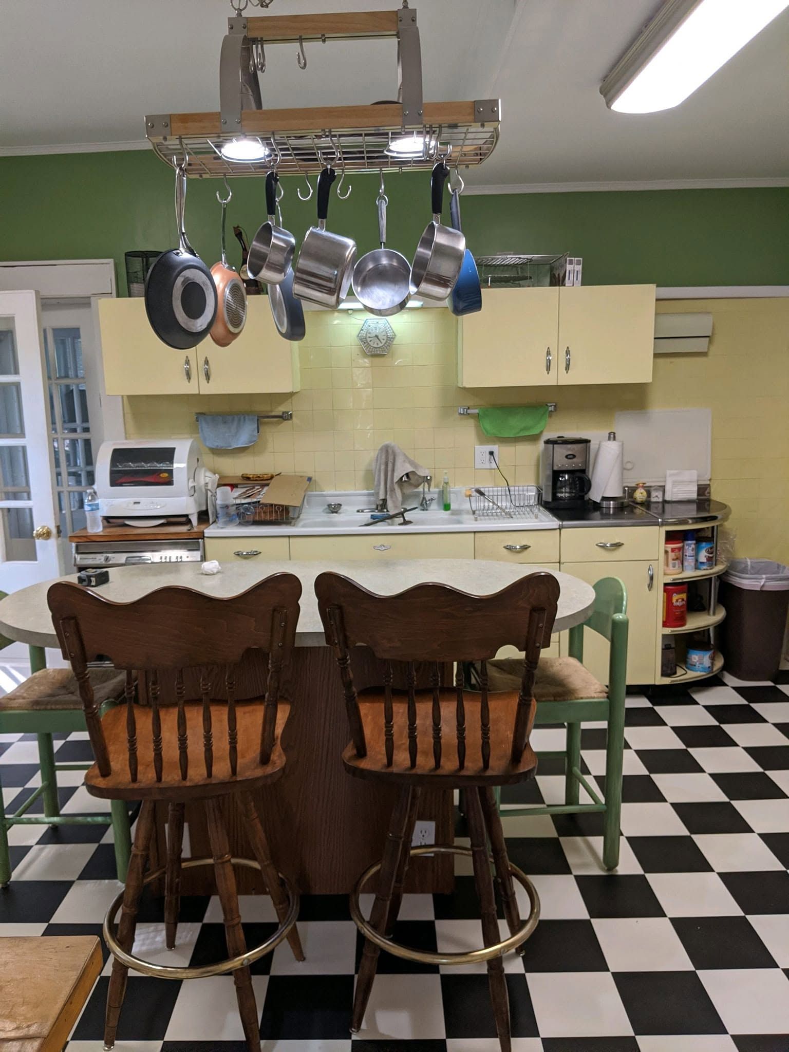 Kitchen with hanging pots, checkered floor, and wooden dining chairs around a table