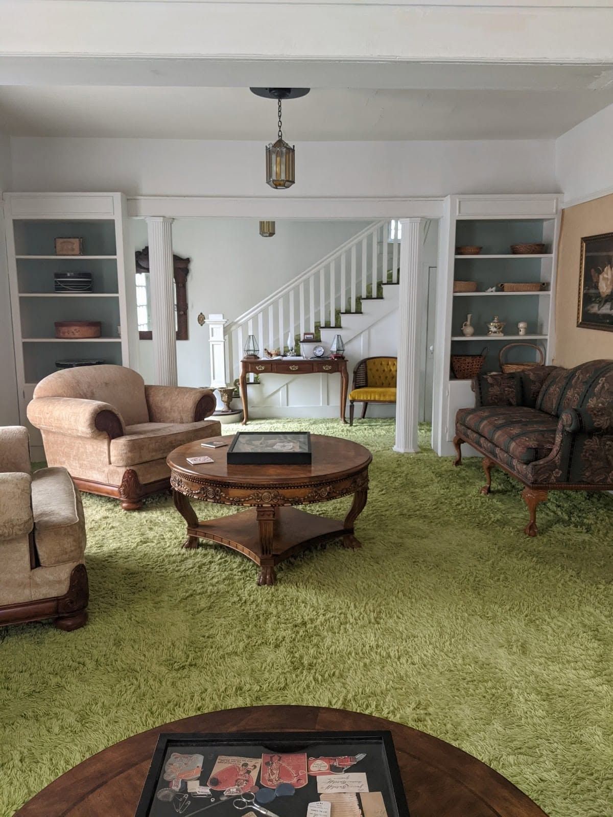 Living room with green carpet, armchairs, coffee table, staircase, and built-in shelves