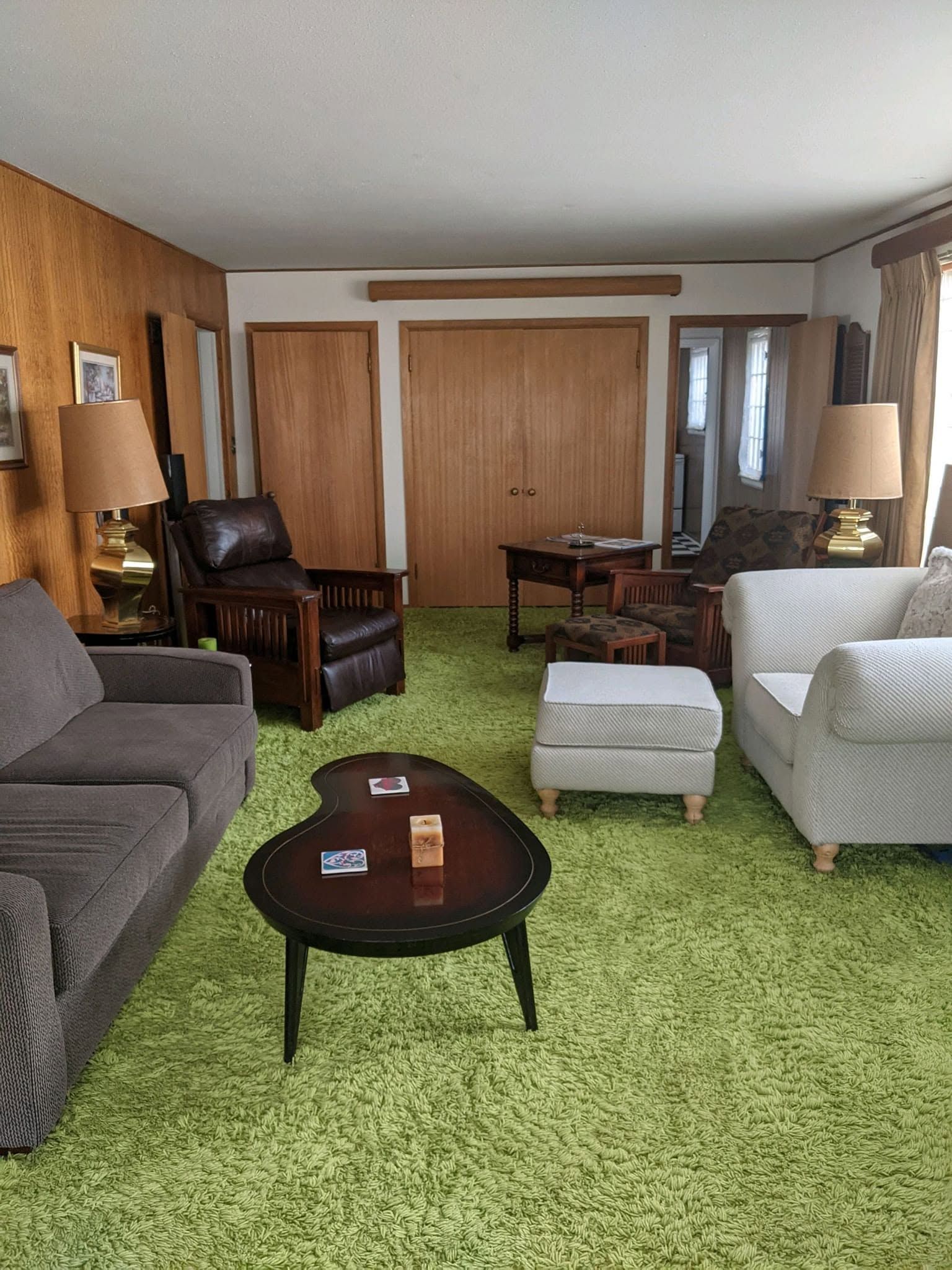 Living room with green carpet, wood-paneled walls, sofa, chairs, coffee table, and lamps