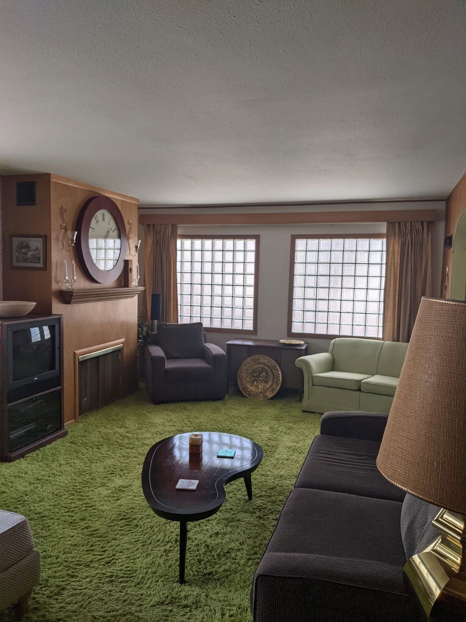 Cozy living room with green carpet, sofa, armchair, coffee table, fireplace, and two windows.