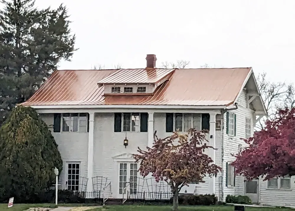 Large white house with a copper roof and dormer windows, framed by trees and shrubs.