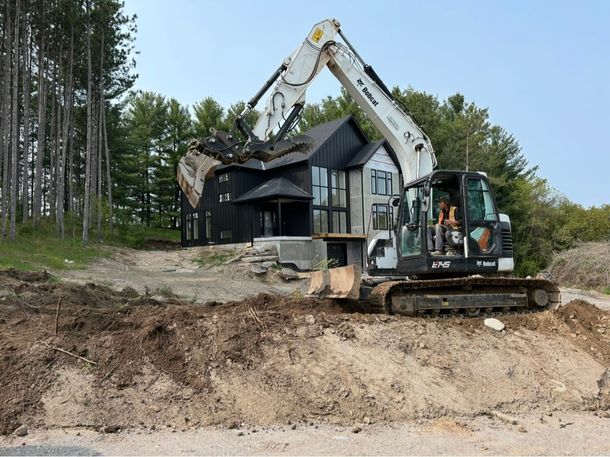 A white excavator performing exterior work in front of a modern two-story house 