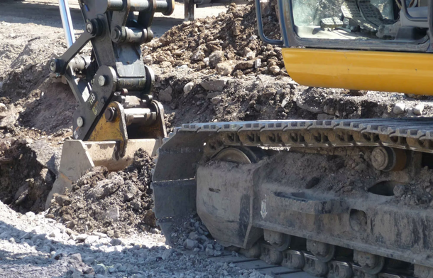 A yellow excavator with metal tracks digging into soil at a construction site