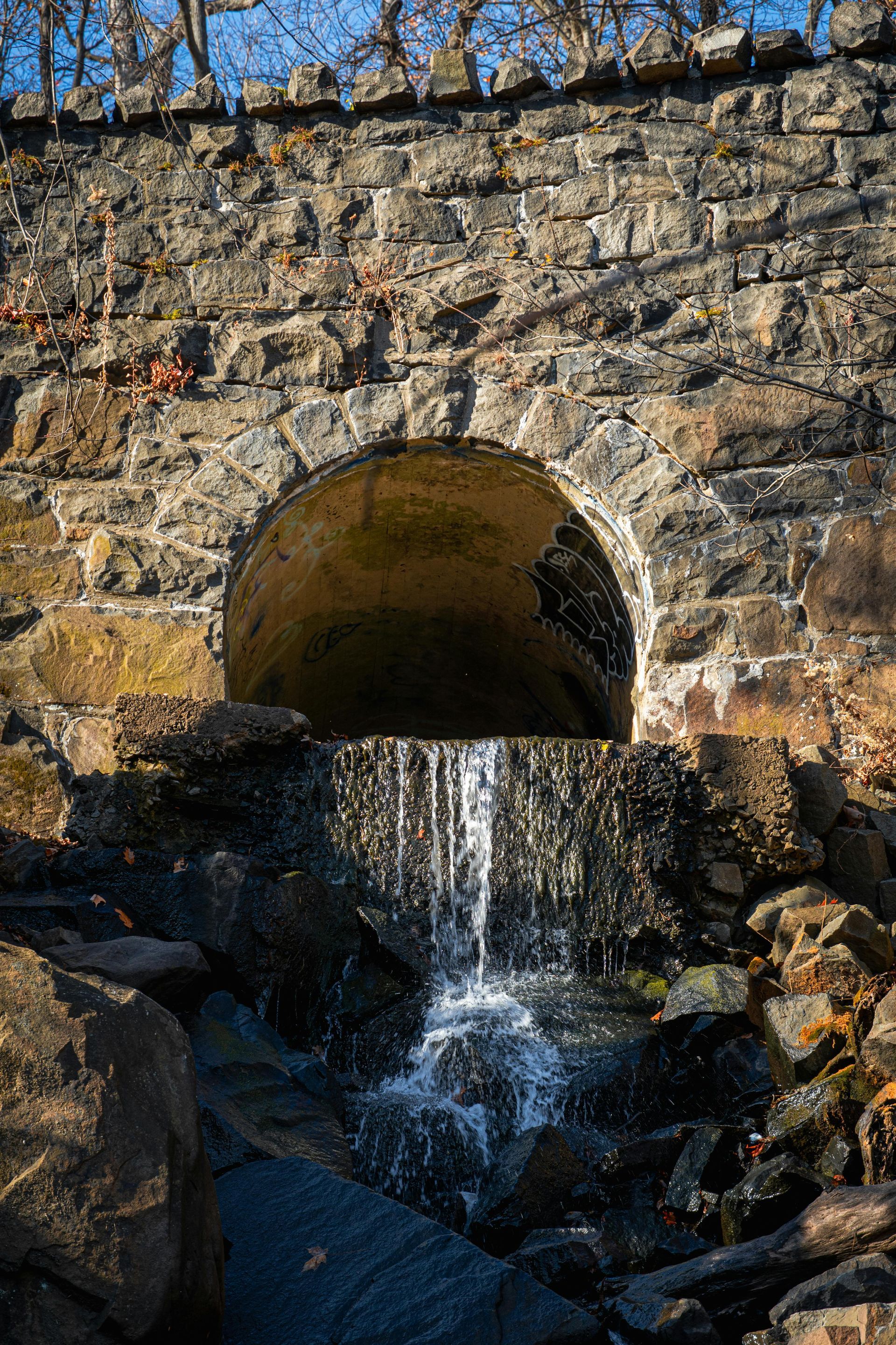 Water trickles from a stone arch culvert down over rocks into a small stream