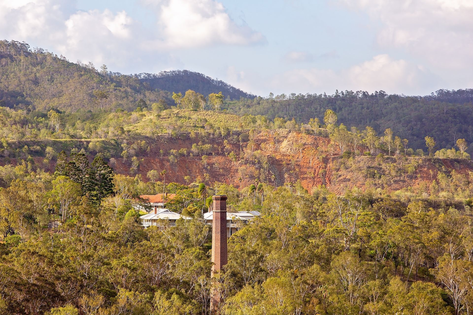 Mountain landscape with reddish earth, trees, and a house with a chimney — Bad Bugs Pest Control in Gracemere, QLD