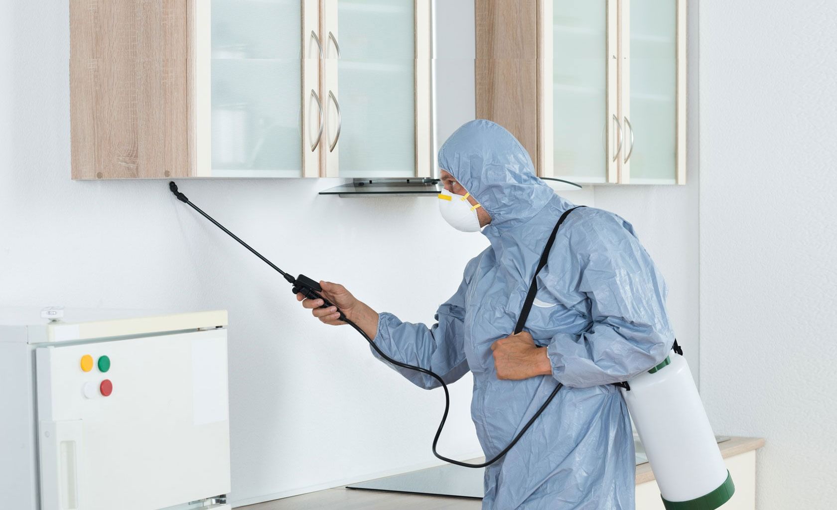 Pest Control Worker in Protective Suit Spraying a Kitchen — Bad Bugs Pest Control in Mount Morgan, QLD