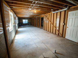 Unfinished basement with exposed beams, concrete floor, insulation, and a white door at right.