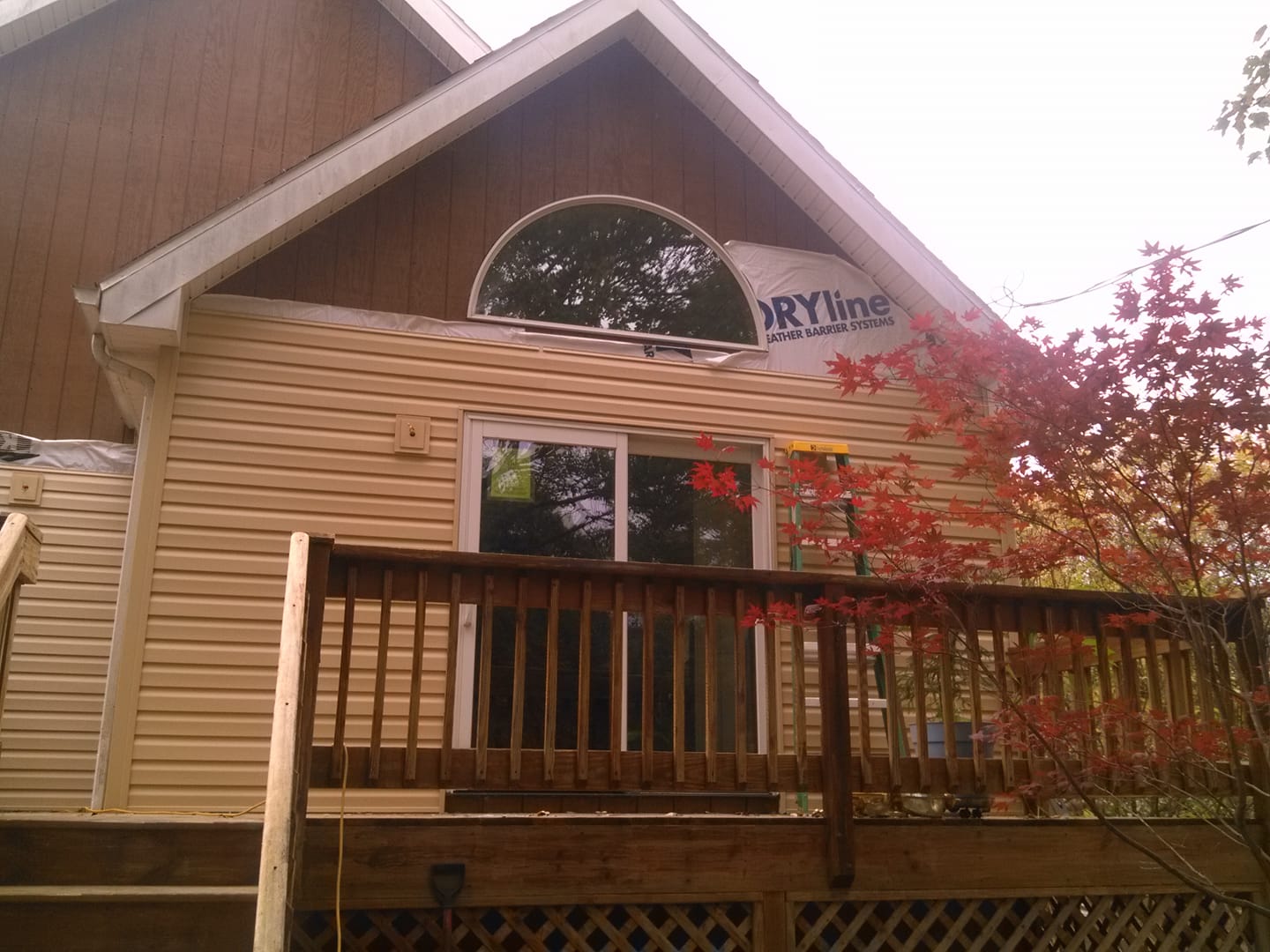 Wooden cabin with a front deck and railing, framed by trees and a large arched window.
