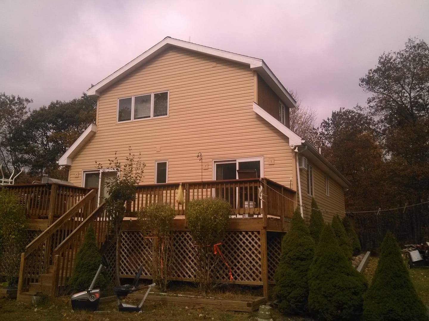 Two-story tan house with a wooden deck and lattice skirting, viewed from the backyard.
