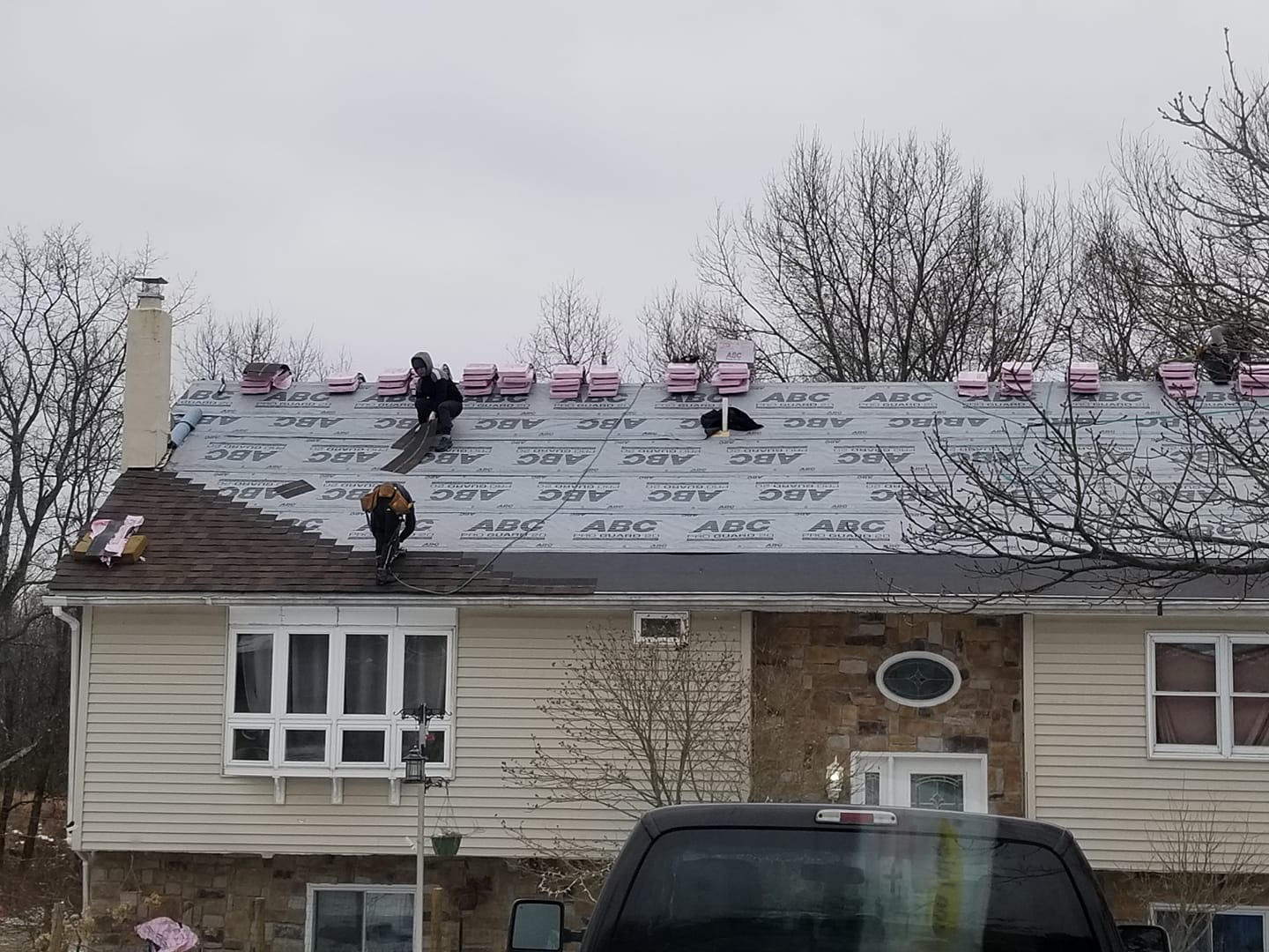 Snow-covered house roof with workers shoveling or repairing it, and a black car parked below.