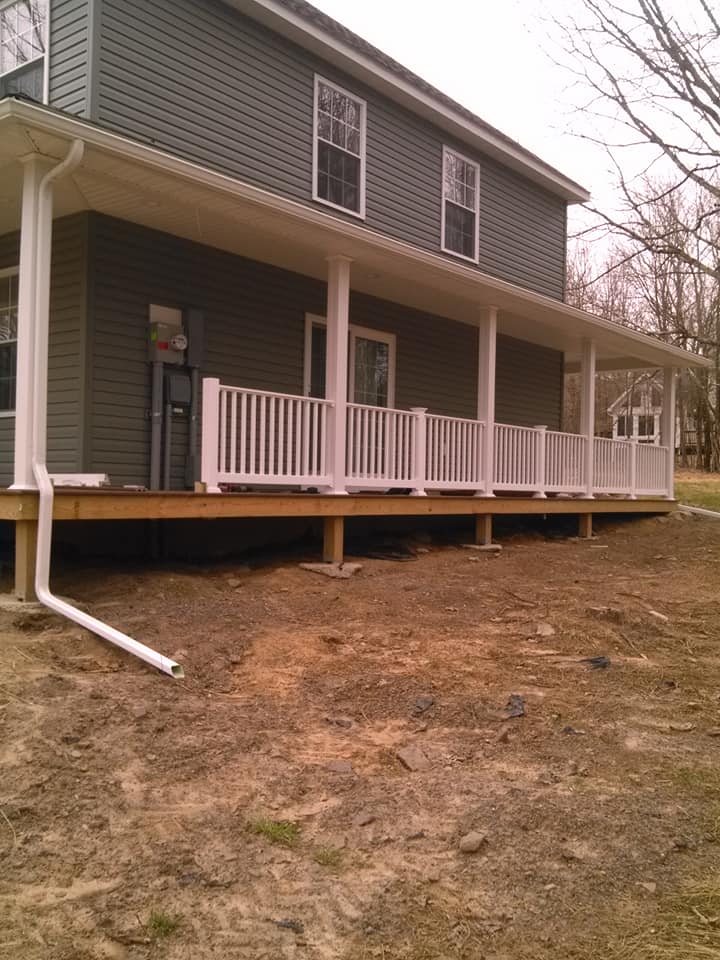 Two-story gray house with a covered porch and white railing on a bare yard slope