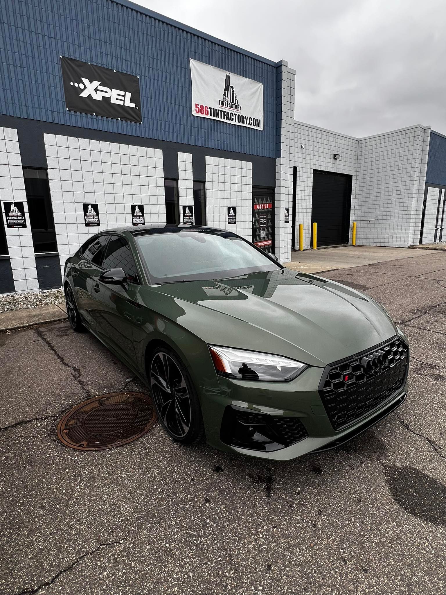 Green sports car parked outside a building with XPEL signage on an overcast day