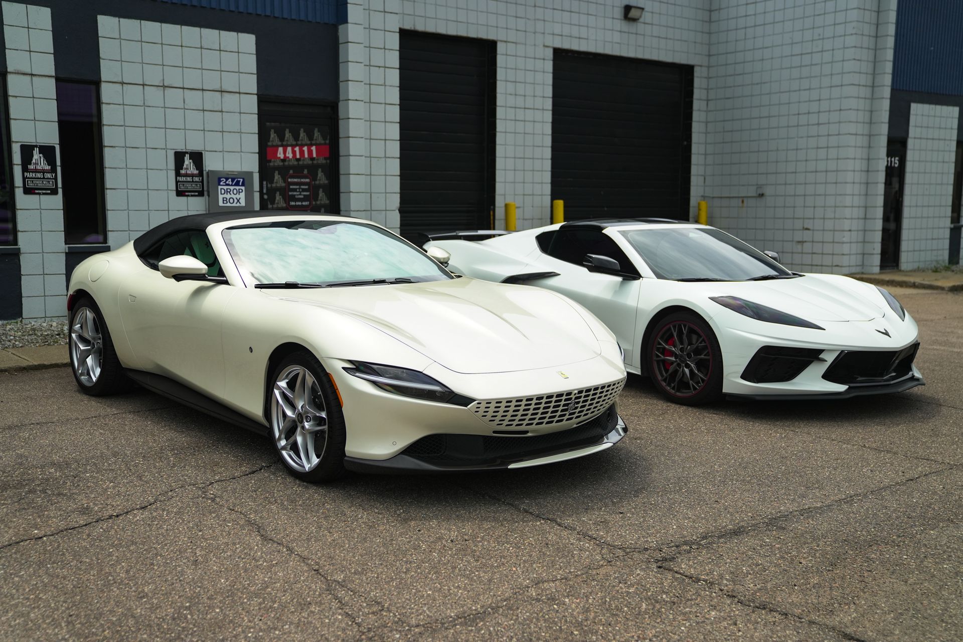 Two white sports cars parked outside a building with garage doors.