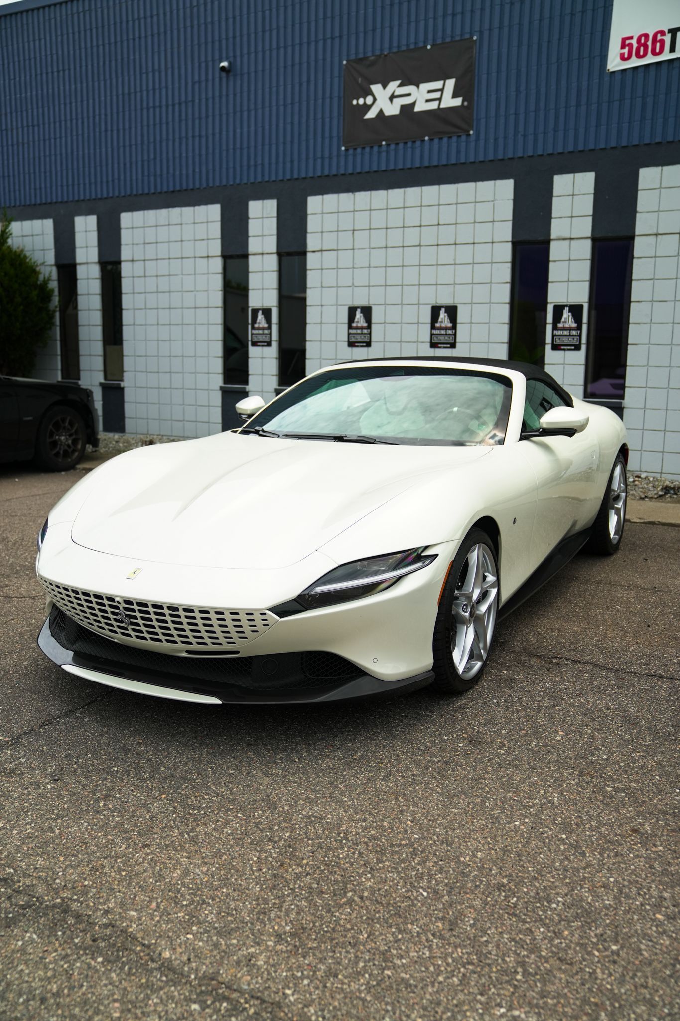 White sports car parked outside a building with glass doors and a dark blue facade.