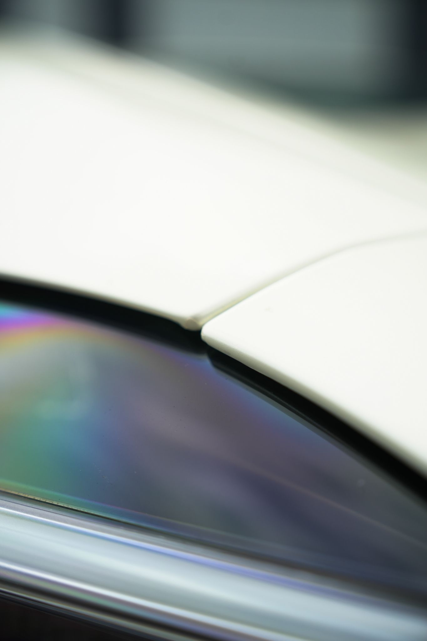 Close-up of a white car body and a reflective tinted window with a rainbow sheen